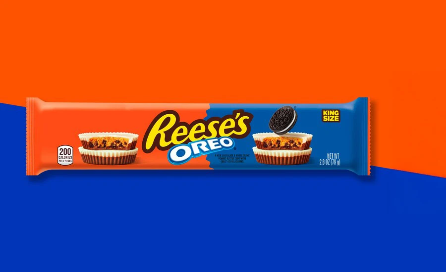 Reeses Oreo King Size candy package displayed on a bold orange and blue background, featuring two peanut butter cups with Oreo cookie pieces inside and an Oreo cookie on top. The package includes the text Reeses Oreo and King Size, creating a playful and energetic mood.