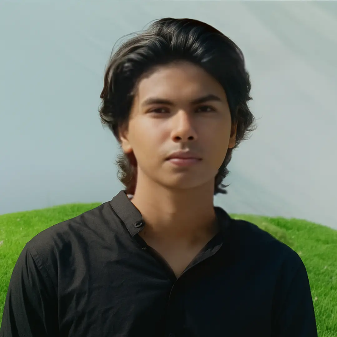 Young man named Linshad with medium-length dark hair wearing a black shirt standing outdoors on a grassy area with a light sky in the background, presenting a calm and confident demeanor